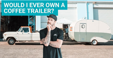 Jimmy Evans the youtube presenter on Artisti Coffee Roasters channel is standing with a questioning look on his face in front of a coffee caravan asking the question "Would I ever own a coffee trailer"?