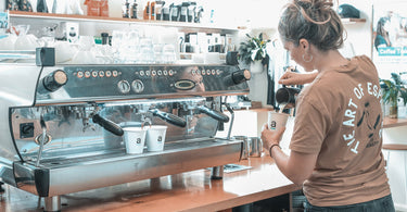 A female barista working at an espresso bar in Coffs Harbour that has a La Marzocco 3 group coffee machine.